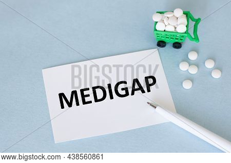 On White A Card With The Text Medigap On A Blue Background Near A Pen And White Pills