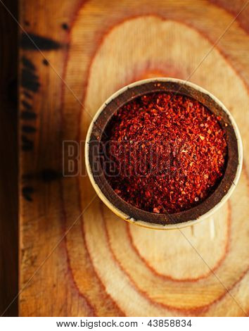 Red hot chilli pepř vločky v misce na dřevěném prkénku pozadí, mělké dof