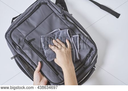 Cleaning Backpack With Washcloth. A Person Wipes Off Dirt Or Dust From The Outside Of The Bag. Wipin