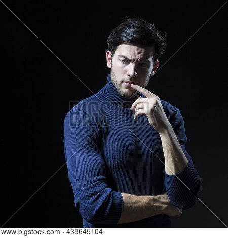 Thinking Handsome Brunet Man Posing In Blue Turtle Neck Sweater With Folded Hands Against Black Back
