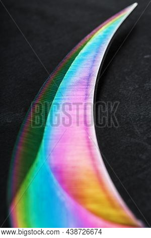 The Curved Sharp Blade Of The Kerambit Dagger Is A Gradient Rainbow Color On A Dark Background.