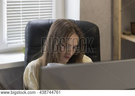 Portrait Young Woman In Glasses With Cup Behind Monitor. Secretar On Working Place. Chief Is Reading