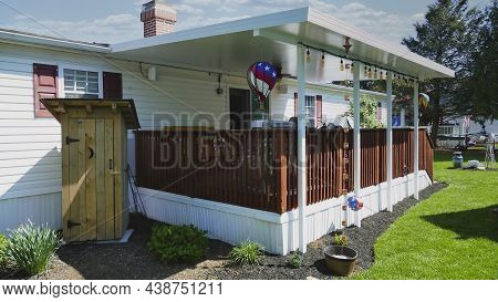 Mobile, Manufactured, Modular, Prefabbed Home With A Deck And Outhouse On A Sunny Day