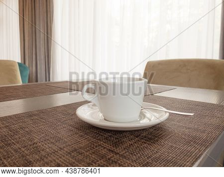 A White Cup Of Tea With A Saucer Is On The Table, Behind Is A Window. Copspace