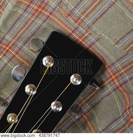 Musical Instrument - Top View Headstock Peghead Black Acoustic Guitar On A Cloth Fiber Plaid Backgro