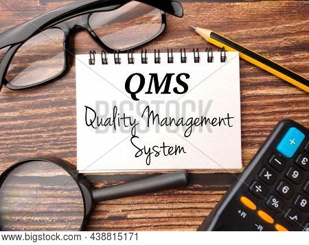 Magnifying Glass,glasses,calculator,pencil And Notebook With Text Qms Quality Management System On A