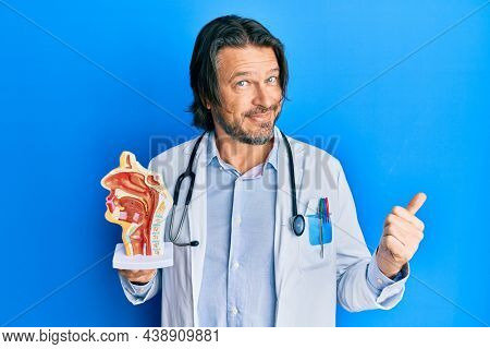 Middle age handsome otologist doctor man holding medical model pointing thumb up to the side smiling happy with open mouth 