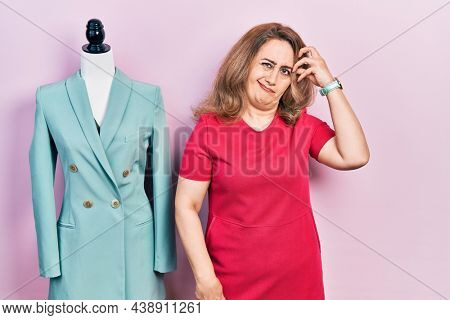 Middle age caucasian woman standing by manikin worried and stressed about a problem with hand on forehead, nervous and anxious for crisis 