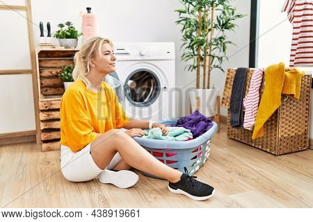 Young caucasian woman putting dirty laundry into washing machine looking to side, relax profile pose with natural face and confident smile. 