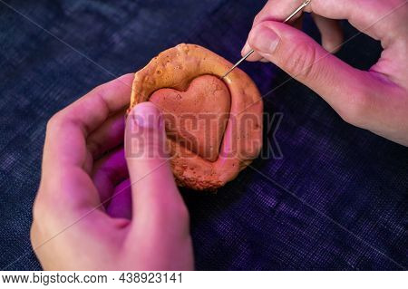 Hands closeup scratch brown sugar caramel candy cookies with a metal needle in the shape of a heart on a white backgound