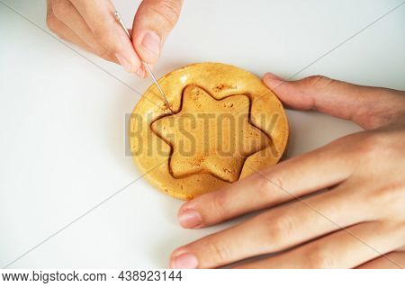 Hands closeup scratch brown sugar caramel candy cookies with a metal needle in the shape of a star on a white background.