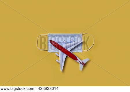 Airplane Toy Model And Face Mask On Yellow Background. New Flight Rules Or Travel Restrictions. Plan