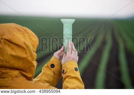 Farmer With Hood On Head Holding Rain Gauge After Heavy Rain In Field In Spring Time