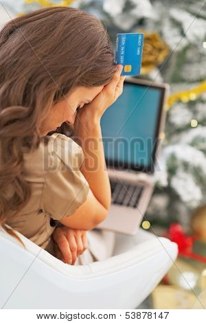 Stressed Young Woman With Credit Card And Laptop In Front Of Christmas Tree