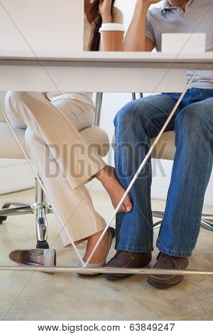 Casual businesswoman playing footsie with colleague under desk in the office