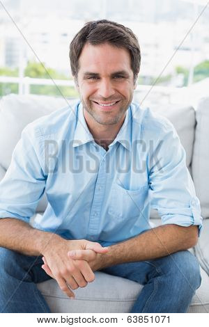 Happy handsome man sitting on the couch looking at camera at home in the living room
