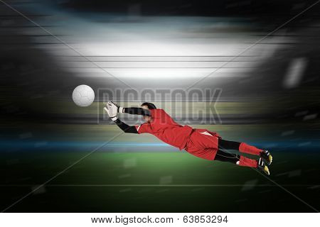 Fit goal keeper jumping up in a large football stadium with lights
