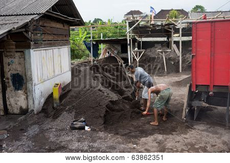 BALI - APRIL 11, 2014:Two unidentified laborers scoop volcanic sand onto a truck in Bali, Indonesia. Volcanic sand from past eruptions has commercial value and industrial use as construction material.