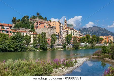 Shallow stream and riverbed overgrown with trees and shrubs along old town of Ventimiglia, Italy.