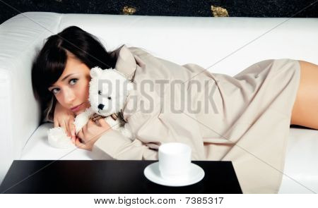 The young girl lying on a sofa with teddy bear toy
