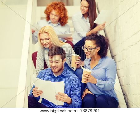 business, office and startup concept - smiling creative team with papers and take away coffee on staircase