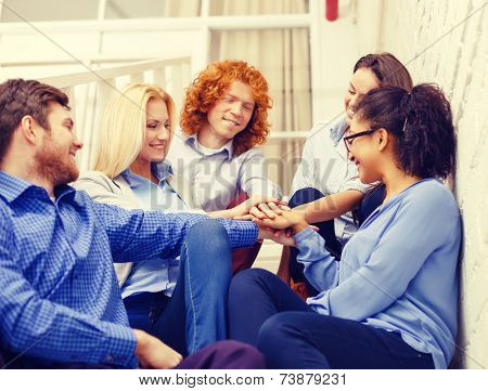business, office, gesture and startup concept - smiling creative team with hands on top of each other sitting on staircase