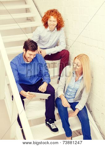 business, technology and startup concept - smiling creative team with tablet pc computer sitting on staircase