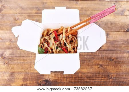 Fried noodles and sticks in takeaway box on wooden background