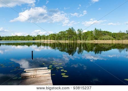 White Clouds On The Blue Sky Over Blue Lake With Boats And Boardwalk