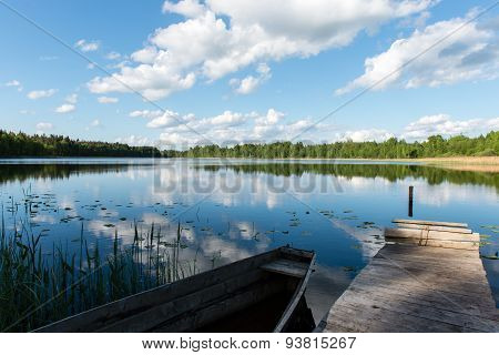White Clouds On The Blue Sky Over Blue Lake With Boats And Boardwalk