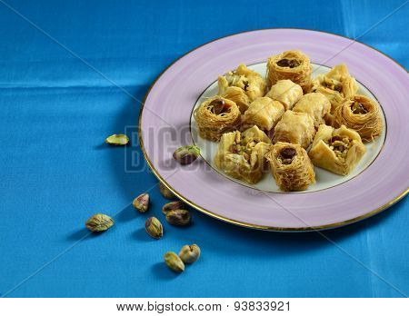 Baklawa in a plate with few whole pistachio nuts scattered on blue background.