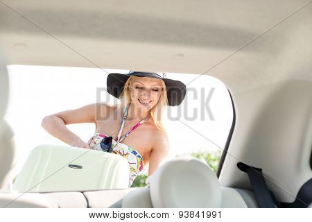 Happy woman loading suitcase in car trunk