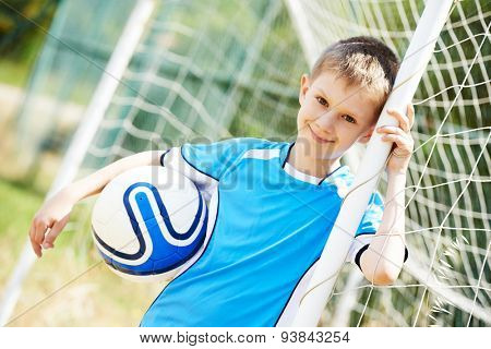 Happy smiling young boy with football ball standing near gates