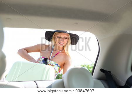 Happy woman loading suitcase in car trunk