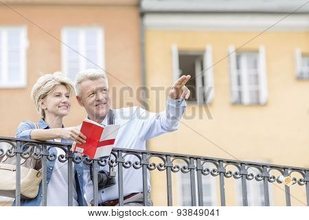 Happy man showing something to woman with guidebook in city