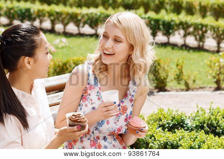 Two girlfriends in park with coffee and cupcakes