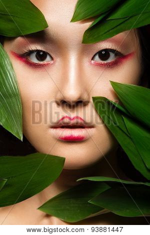 Beautiful Asian girl with a bright make-up art in green leaves. Beauty face. Creative image.