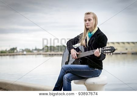 Cute Blonde Playing Guitar While Sitting On The Bitt