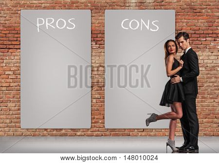 pros and cons in a relationship, young elegant couple standing embraced near big posters 