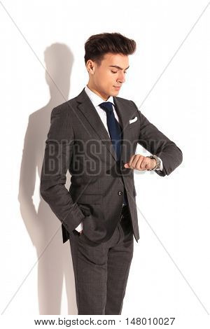 young business man cheking time on his watch, studio picture on white wall