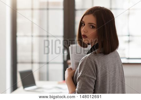 Young businesswoman in half turn in office, holding documents, close-up. Busy business woman in office with papers