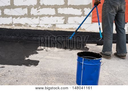 Worker covered surface bitumen primer for improving adhesion during surfacing rolled waterproofing during the installation of isolation on industrial or household objects