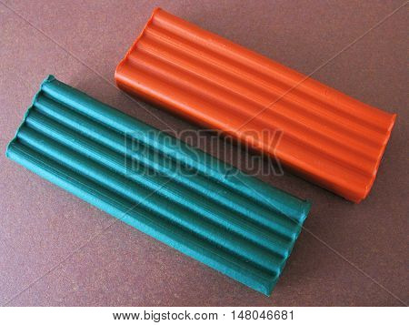 Plasticine on brown paper. Plasticine on brown background. Green plasticine. Orange plasticine. Plasticine on colored paper. The plasticine on the paper background. Modeling clay. School supplies. Supplies for creativity.