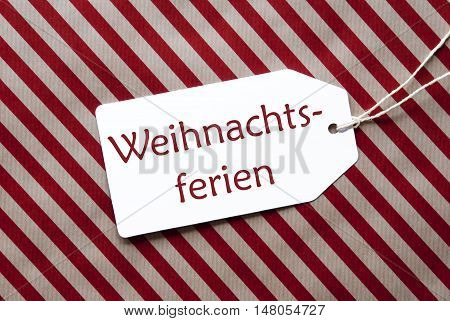 One Label On A Red And Brown Striped Wrapping Paper. Textured Background. Tag With Ribbon. German Text Weihnachtsferien Means Christmas Break