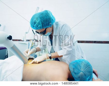 Laser treatment. Caucasian doctor making laser procedure skin nevus removal to woman patient.