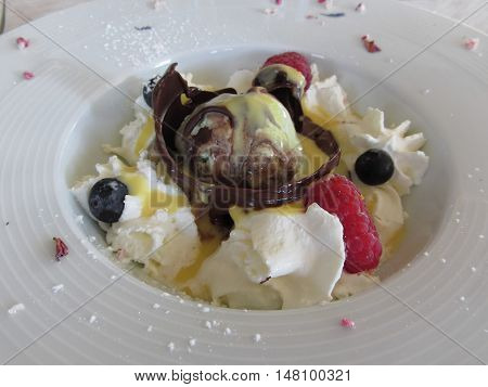 Melted chocolate ball with zabaglione cream whipped cream raspberries and blueberries