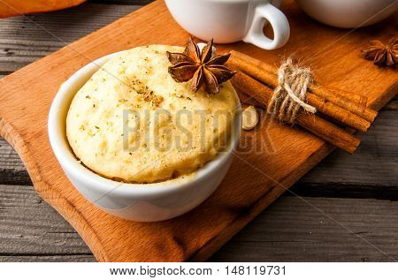 Pumpkin mug-cakes in rustic style, on an old wooden table, next to the cuted pumpkins and spices, close view, copy space