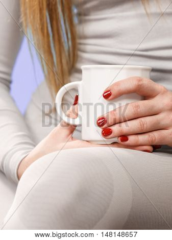 Woman in winter gray sports thermal underwear for skiing training holds mug with tea or coffee warming herself studio shot