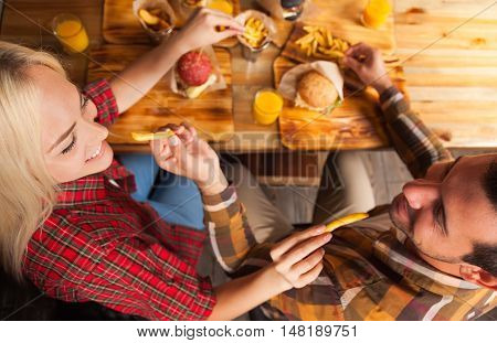 Young Man And Woman Eating Fast Food Potato Sitting At Wooden Table In Cafe Top Angle View, Friends Meeting Communication