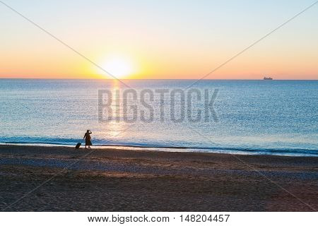 Around the World Exotic Vacation Concept Silhouette of Female pulling Travel Suitcase along Ocean Beach Luminous Sunrise on Background